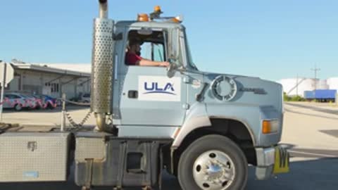 Close-up tracking shot of the side and wheels of a ULA semi-truck driving outdoors.