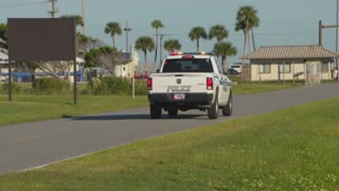 Medium tracking shot of a police car driving down a paved road lined with trees.