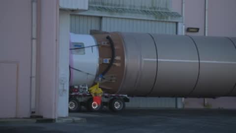 A medium shot shows the front of a rocket booster entering a hangar.