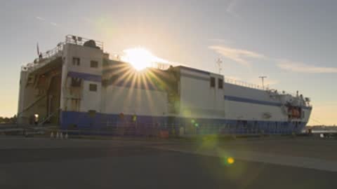 Static wide shot of a cargo ship moored by the dock at sunrise.