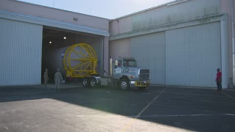 A medium shot shows a truck pulling a rocket booster into a hangar.