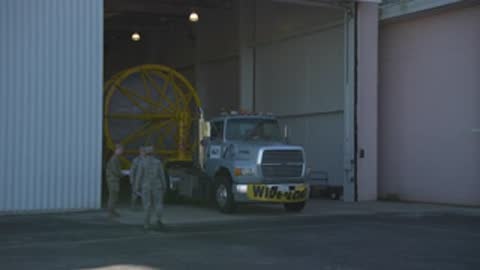 A medium shot shows a truck carrying a rocket booster stopping inside a hangar.