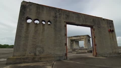 Medium shot of a thick concrete wall with circular portholes and a doorway