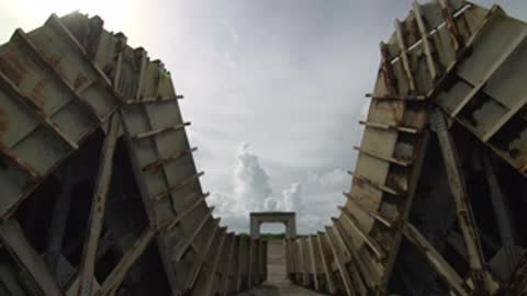 Looking up between two curved metal walls toward a distant cloud formation