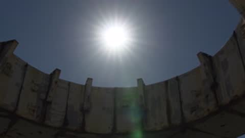 Close-up looking up at the sun through a circular concrete structure.
