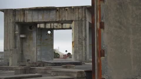Medium shot inside a concrete ruin looking towards an exit.