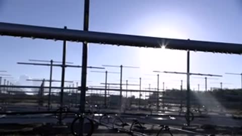 Medium shot looking upward through metal scaffolding toward the bright sun and clear sky.