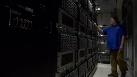 Medium shot of a worker inspecting and interacting with server racks in a brightly lit data room.