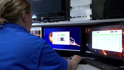 Medium shot from the side of a person working at computer monitors displaying charts and data.