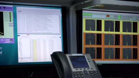 Close-up of several monitors displaying various charts, graphs, and data outputs in a control room.