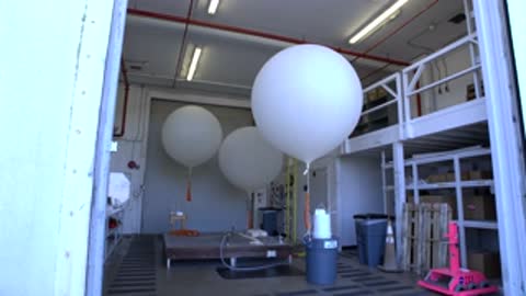 Medium shot inside a building with two large white weather balloons and equipment.