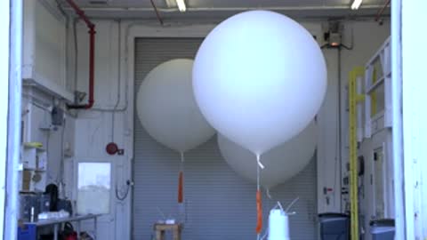 Close-up of a large white weather balloon inflating inside a workshop environment.
