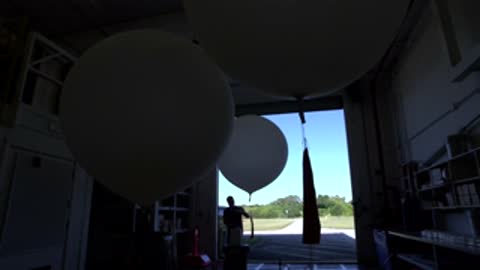 Medium shot of a large weather balloon silhouetted against the bright doorway leading outside.