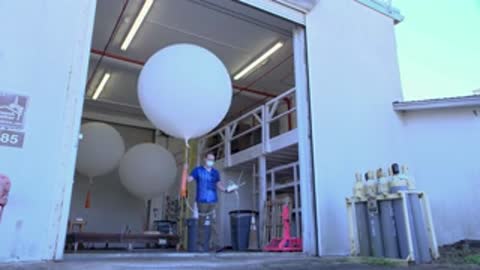 man carrying a weather balloon walking out of a hangar