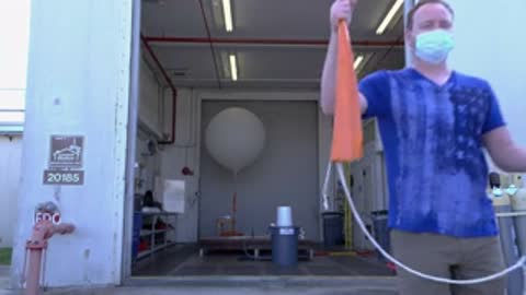 man holding a weather balloon and an orange parachute outdoors