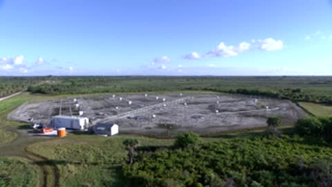 Aerial view of weather monitoring facility surrounded by trees under a clear blue sky.
