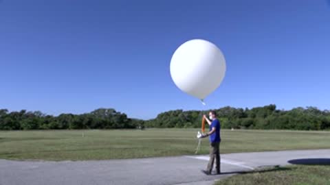man walking across an open field holding a weather balloon
