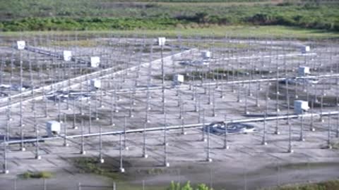 Aerial tracking shot moving over the grid of metal towers and monitoring equipment.