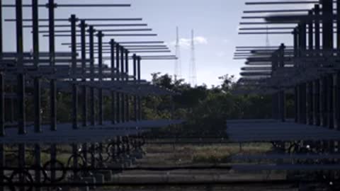 Medium shot looking down rows of metal structures with horizontal antennas against a hazy sky.
