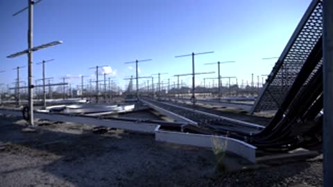 Medium shot of ground-level cable trays and structured metal poles in a sunny clearing.
