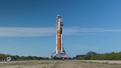 The SLS rocket is transported along the crawlerway on a clear day.