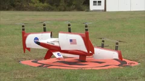 The aircraft takes off vertically from the red launch pad in the field.