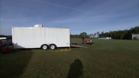 A white trailer is parked on a grassy field under a blue sky.