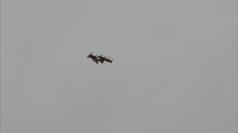 The aircraft flies at a distance against a gray, overcast sky.