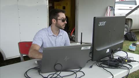A technician working at an outdoor computer setup under a canopy.