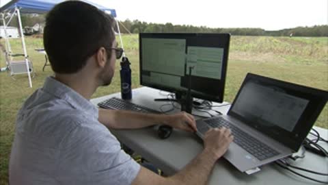 A technician monitoring computer data while sitting outdoors.