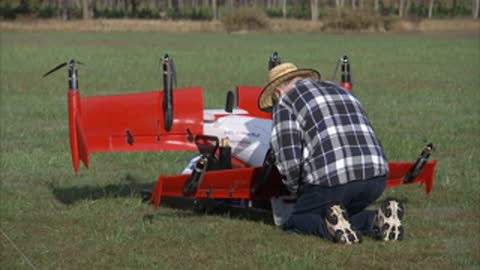 A person in a plaid shirt and straw hat kneels by an aircraft.
