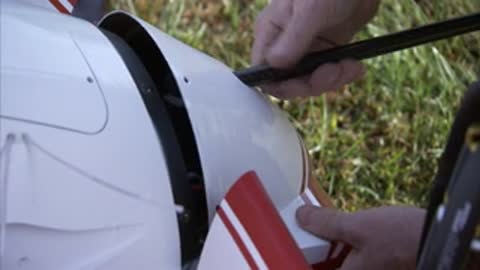 Hands attach a long black rod to the nose of the aircraft.