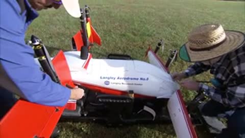 Two people assemble the red and white aircraft on the grass.
