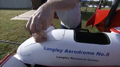A person in a hat works on the nose of the aircraft labeled "Langley Aerodrome No.8".