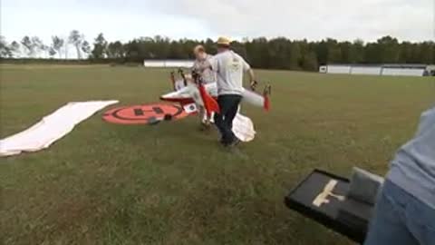 People move the aircraft onto a red launch pad on the grass.