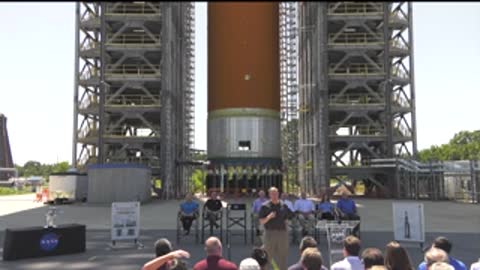 A group of people seated outside in front of a large rocket model.
