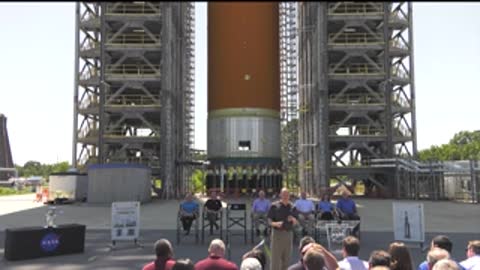 A wider outdoor shot of a group gathered in front of a rocket model.