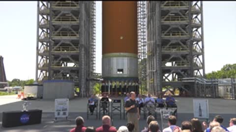 Wide shot of people seated outside in front of a large rocket model.