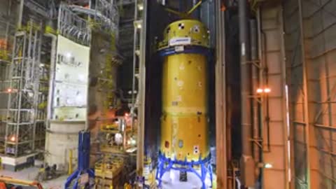Medium vertical shot inside a tall industrial structure with a cylindrical rocket section.