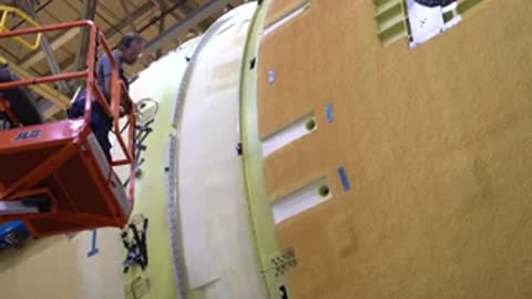 Close-up tracking shot of a worker on a lift inspecting a textured rocket structure.