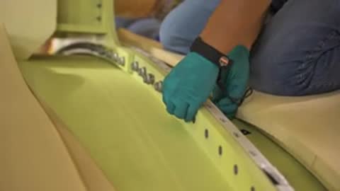 Close-up shot of a worker's hands using a tool on a component's interior surface.
