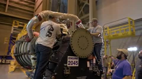 Medium shot of technicians working on a rocket engine part inside a workshop.