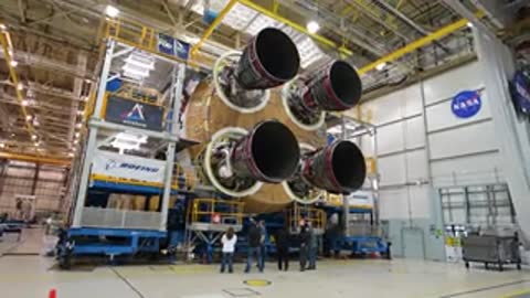 Wide shot of four rocket engines attached to the main assembly inside a large hall.