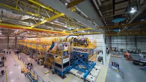Wide overhead shot of a completed rocket stage inside a large industrial manufacturing facility.