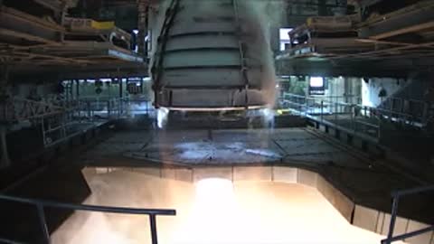 Medium shot inside a facility as a rocket engine fires with bright light and smoke.