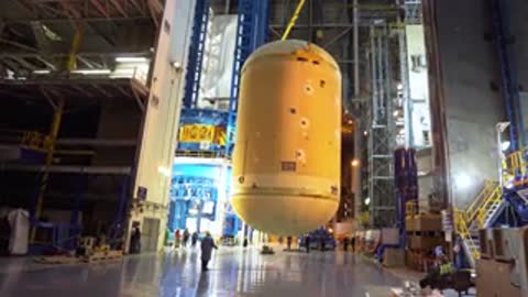 Medium shot inside a factory as a large cylindrical container is lifted by a crane.