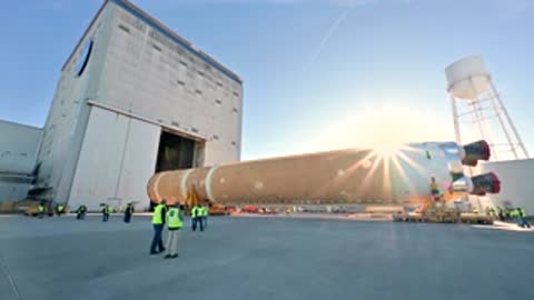 Rocket stage transport moving past building in bright sunlight