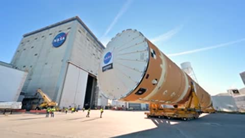 Large rocket stage moving past manufacturing building exterior
