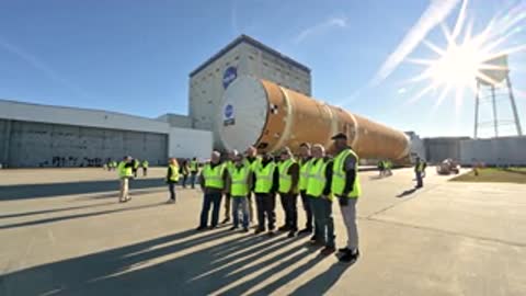 Workers in high visibility vests standing near moving rocket stage