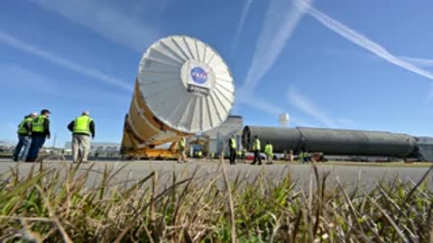 Rocket stage transport passing storage area with pipes outside